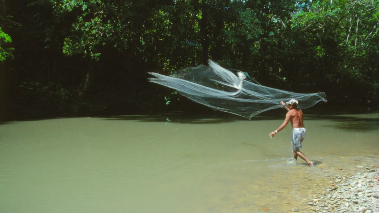 Der fiskes med net i regnskoven nær et langhus. Foto Hanne Christensen