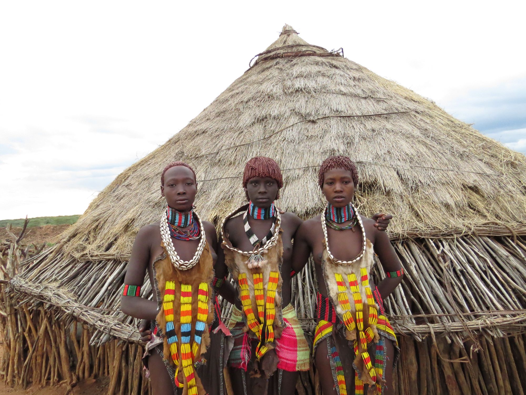 Tre unge kvinder fra Hamer-folket foran traditionel stråtækt hytte i Omodalen i det sydlige Etiopien. Foto Esben Gynther